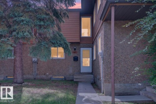 Two-story exterior with textured siding, accent wood-finish siding, white framed windows, and a concrete walkway - #47 3812 20 Av Nw, Edmonton, AB 