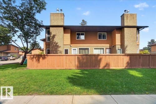 Modern multi-level residence featuring a distinctive architectural design with stacked stone chimney elements, warm-toned exterior siding, and horizontal wood-finish fencing - #47 3812 20 Av Nw, Edmonton, AB 