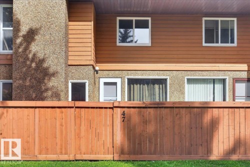 Wood panel fencing enclosing a manicured lawn, featuring a multi-story exterior with horizontal siding and textured wall finishes, and multiple windows with white frames - #47 3812 20 Av Nw, Edmonton, AB 