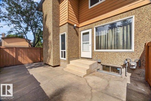 Concrete patio area featuring a wooden privacy fence, textured exterior siding, and multiple windows - #47 3812 20 Av Nw, Edmonton, AB 