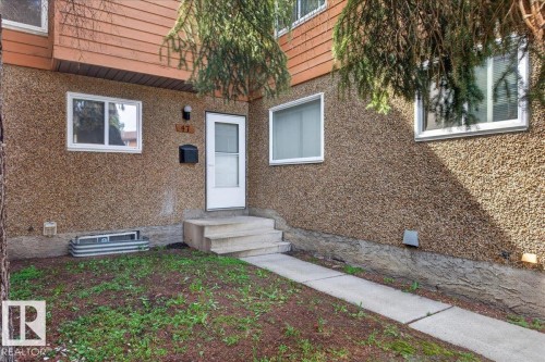 Stucco exterior with upper-level wood paneling, front entry door with glass insert, concrete walkway, and exterior lighting - #47 3812 20 Av Nw, Edmonton, AB 