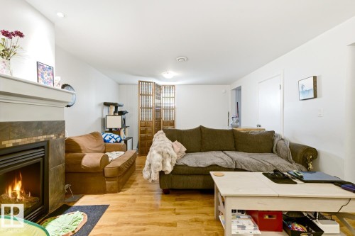 Basement Living room - Fireplace with stone and tile surround, wood-finish flooring, recessed lighting, and white walls - 9740 63 Avenue Nw, Edmonton, AB 