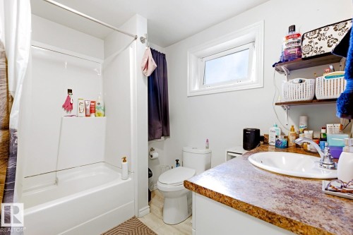 Bathroom featuring a wood-finish vanity with a vessel sink, stone countertop, and ample storage - 9740 63 Avenue Nw, Edmonton, AB 