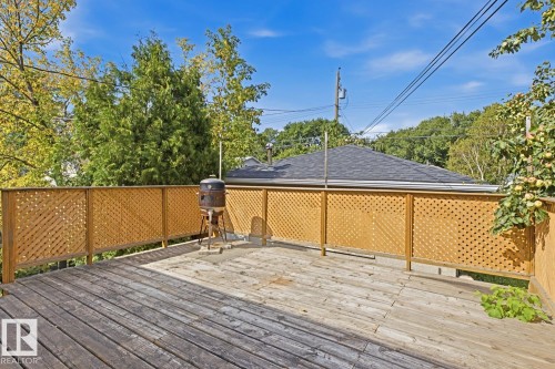 Spacious composite deck with wood-finish flooring and lattice privacy fencing, overlooking mature landscaping and tree-lined surroundings - 9740 63 Avenue Nw, Edmonton, AB 