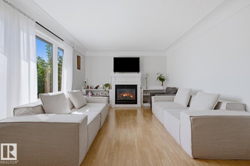 Bright, open living area featuring gleaming wood-finish flooring, dual upholstered seating arrangements, and expansive windows with natural light - 9740 63 Avenue Nw, Edmonton, AB 