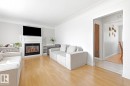 Bright open-concept living area featuring hardwood flooring, a gas fireplace with built-in cabinetry, and a wall-mounted flat-screen television - 9740 63 Avenue Nw, Edmonton, AB 