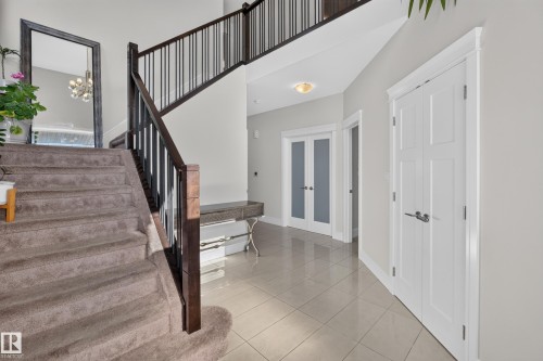 Two-story entry featuring a carpeted staircase with dark wood and black metal railings, tiled flooring, and modern lighting - 3685 Claxton Place Sw, Edmonton, AB 