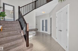 Two-story entry featuring a carpeted staircase with dark wood and black metal railings, tiled flooring, and modern lighting - 