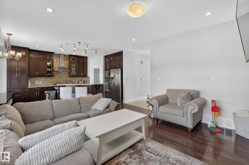Open-concept living area featuring rich wood-finish flooring, recessed lighting, and a modern kitchen - 3685 Claxton Place Sw, Edmonton, AB 