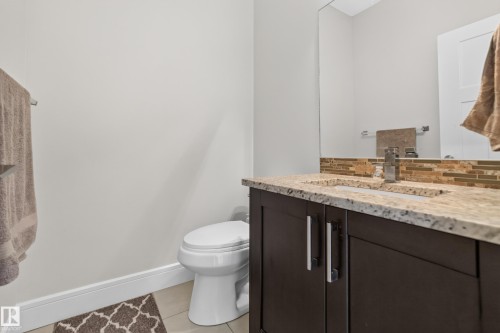 Dark wood-finish vanity with dual-handle hardware, light-toned countertop with integrated sink, and a tiled backsplash - 3685 Claxton Place Sw, Edmonton, AB 
