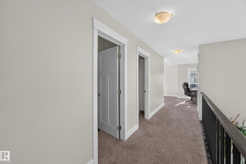 Hallway with neutral wall paint, carpet flooring, multiple doorways, and ceiling-mounted light fixtures - 3685 Claxton Place Sw, Edmonton, AB 