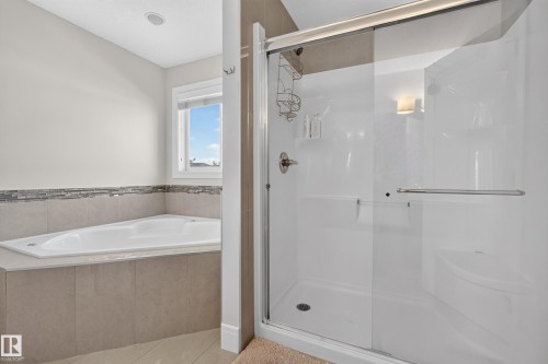 Built-in corner soaking tub with tile surround, mosaic accent tile, and an adjacent glass-enclosed shower with a built-in bench - 3685 Claxton Place Sw, Edmonton, AB 