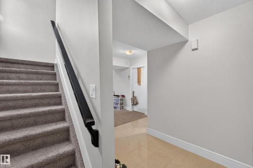 Carpeted staircase with a black handrail and a lower level featuring tile flooring - 3685 Claxton Place Sw, Edmonton, AB 