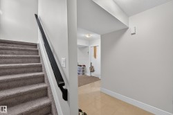 Carpeted staircase with a black handrail and a lower level featuring tile flooring - 