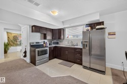 Compact kitchen featuring dark wood-finish cabinetry, stainless steel appliances, a white tile backsplash, and light-toned countertop surfaces - 