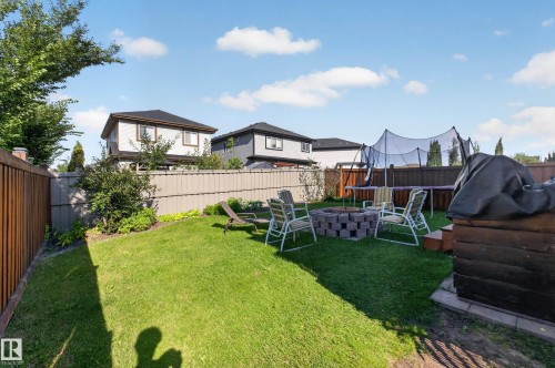 Expansive backyard featuring a manicured lawn, established perimeter landscaping, and a built-in stone fire pit - 3685 Claxton Place Sw, Edmonton, AB 
