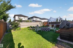 Expansive backyard featuring a manicured lawn, established perimeter landscaping, and a built-in stone fire pit - 