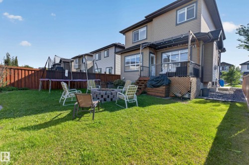 Expansive backyard featuring a manicured lawn, a built-in fire pit, and a raised wooden deck with railings - 3685 Claxton Place Sw, Edmonton, AB 