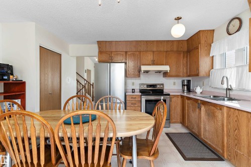 Warm wood cabinetry and stainless steel appliances define this bright kitchen, featuring ample counter space, a center island with wood-finish countertop, and abundant natural light from multiple windows - 17724 94 Street Nw, Edmonton, AB 