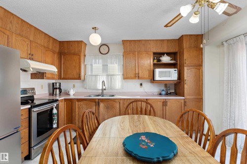 Warm wood cabinetry throughout the kitchen features ample storage and counter space, complemented by stainless steel appliances and a ceramic sink - 17724 94 Street Nw, Edmonton, AB 