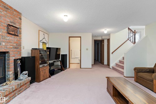 Spacious living area featuring a brick fireplace with hearth, wood-finish cabinetry, carpeted flooring, and a staircase with wood railings - 17724 94 Street Nw, Edmonton, AB 