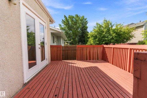 Spacious composite deck featuring rich red-stained wood decking with matching railings and balusters, accessed directly from the home via glass patio doors - 17724 94 Street Nw, Edmonton, AB 