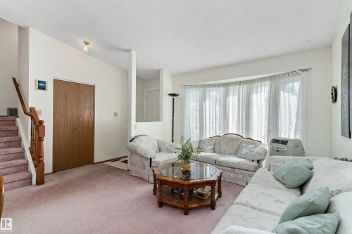 Light-filled living area featuring a large bay window, a wood-finish staircase with balusters, and a built-in closet with wood-finish bi-fold doors - 17724 94 Street Nw, Edmonton, AB 