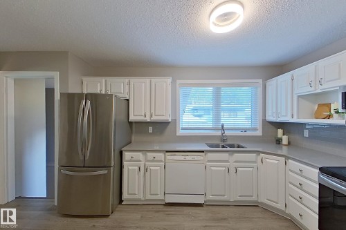 Modern kitchen featuring white cabinetry, gray countertops, a stainless steel refrigerator, white dishwasher, and wood-finish flooring - 16 Brunswick Crescent, St. Albert, AB - Indoor Photo Showing Kitchen With Double Sink