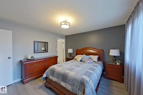 Bedroom featuring light wood-finish flooring, a contemporary ceiling light fixture, a dark accent wall, and sheer window treatments - 16 Brunswick Crescent, St. Albert, AB - Indoor Photo Showing Bedroom