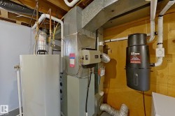 Dedicated utility space featuring a water heater, furnace system, central vacuum unit, and exposed ductwork - 