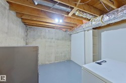 Unfinished basement featuring exposed wood joists, concrete foundation walls, painted concrete flooring, and built-in white cabinetry with open shelving - 