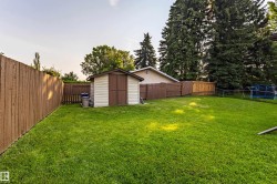 Fenced backyard featuring a storage shed, expansive lawn, mature perimeter trees, and wood fencing - 