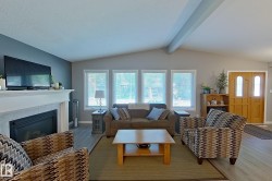 Vaulted ceiling living room featuring a white mantel fireplace with tile surround, wood-finish flooring, and a double-door entryway with arched glass inserts - 