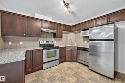 Kitchen featuring dark wood-finish cabinetry, light-toned stone-finish countertops, stainless steel appliances, and a tiled backsplash - 