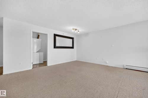 Carpeted interior with white walls, a visible laundry area with stacked appliances, and a ceiling-mounted light fixture - #6430 7331 South Terwillegar Dr Nw, Edmonton, AB 