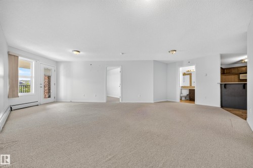 Neutral-toned wall-to-wall carpeting throughout, white painted walls, a glass paneled exterior door with an adjacent window, and a built-in counter with dark cabinetry - #6430 7331 South Terwillegar Dr Nw, Edmonton, AB 