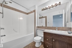 Full bathroom with a white tub-shower combination, tiled surround, wood-finish vanity, and a large wall-mounted mirror with overhead vanity lighting - 