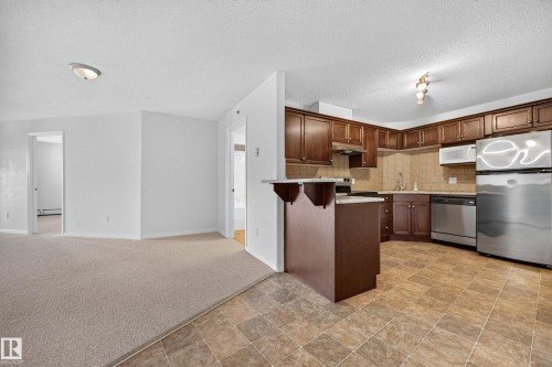 Kitchen featuring wood-finish cabinetry, stainless steel appliances, a tile backsplash, and a breakfast bar - #6430 7331 South Terwillegar Dr Nw, Edmonton, AB 