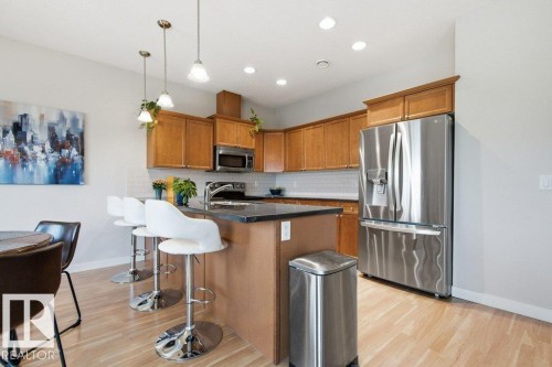 Bright kitchen featuring wood-finish flooring, ample cabinetry, a dark countertop island, stainless steel appliances, and recessed lighting - #17 7293 South Terwillegar Dr Nw, Edmonton, AB - Indoor Photo Showing Kitchen