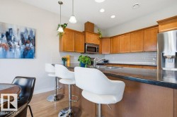 Kitchen featuring warm wood cabinetry, stainless steel appliances, a dark countertop, white subway tile backsplash, and light wood-finish flooring - 