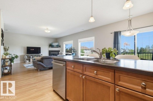 Kitchen island with wood cabinetry, a double basin stainless steel sink, and stainless steel dishwasher - #17 7293 South Terwillegar Dr Nw, Edmonton, AB - Indoor Photo Showing Kitchen With Double Sink