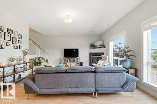 Living area featuring wood-finish flooring, a fireplace with a dark surround and white mantel, and large windows - #17 7293 South Terwillegar Dr Nw, Edmonton, AB - Indoor Photo Showing Other Room With Fireplace