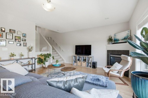 Spacious living area featuring light wood-finish flooring, a contemporary fireplace with a dark tile surround and white mantel, and a staircase with white risers and handrails - #17 7293 South Terwillegar Dr Nw, Edmonton, AB - Indoor Photo Showing Living Room With Fireplace