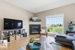 Living area featuring light wood-finish flooring, a corner fireplace with a dark tile surround and white mantel, and a large picture window with grid patterns - 