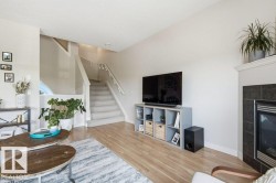 Living space featuring light wood-finish flooring, a carpeted staircase with white railings, a corner-set fireplace with dark tile surround, and neutral wall tones - 