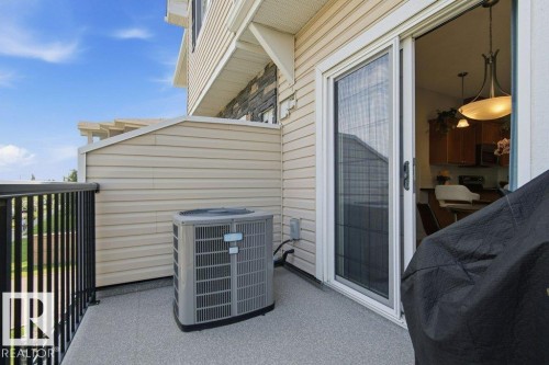 Outdoor balcony featuring a gray speckled floor, black metal railings, and a sliding glass door with a screen - #17 7293 South Terwillegar Dr Nw, Edmonton, AB - Outdoor With Exterior