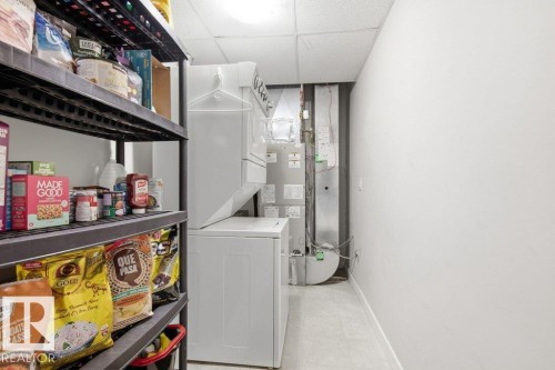 Utility room featuring a stacked washer and dryer, adjacent to built-in shelving, with a drop ceiling and light-toned flooring - #17 7293 South Terwillegar Dr Nw, Edmonton, AB - Indoor Photo Showing Laundry Room