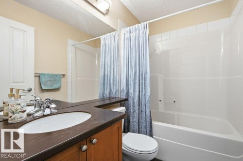 Bathroom featuring a wood-finish vanity with an integrated sink and dark countertop, chrome fixtures, and a white tub/shower combination with white tile surround - #17 7293 South Terwillegar Dr Nw, Edmonton, AB - Indoor Photo Showing Bathroom