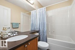 Bathroom featuring a wood-finish vanity with an integrated sink and dark countertop, chrome fixtures, and a white tub/shower combination with white tile surround - 