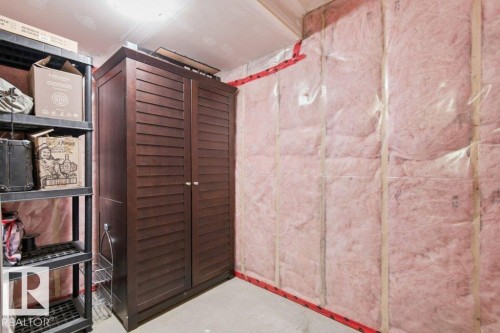 Unfinished room featuring exposed insulation, concrete flooring, and a built-in dark wood storage cabinet with louvered doors - #17 7293 South Terwillegar Dr Nw, Edmonton, AB - Indoor Photo Showing Bathroom